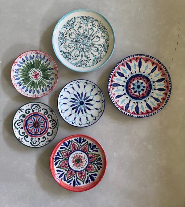 Six ceramic plates featuring intricate hand-painted mandala designs in blue, red, and green on a neutral floor.