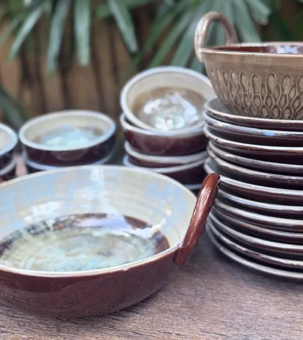 Handmade dark brown ceramic bowls and stacked plates with light blue interior glaze on a wood table.