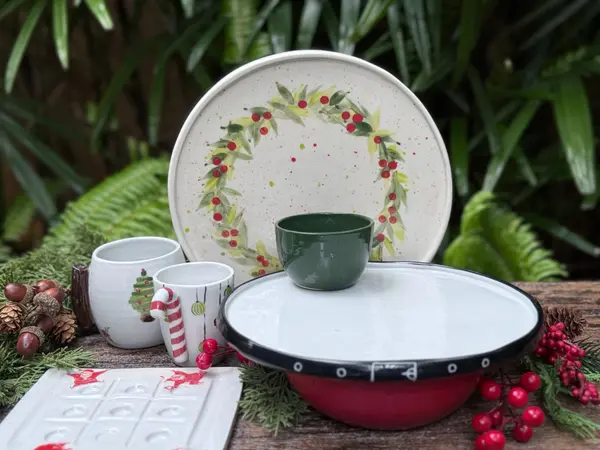 Hand-painted Christmas ceramic collection including a wreath plate, holiday mugs, and a red cake stand.