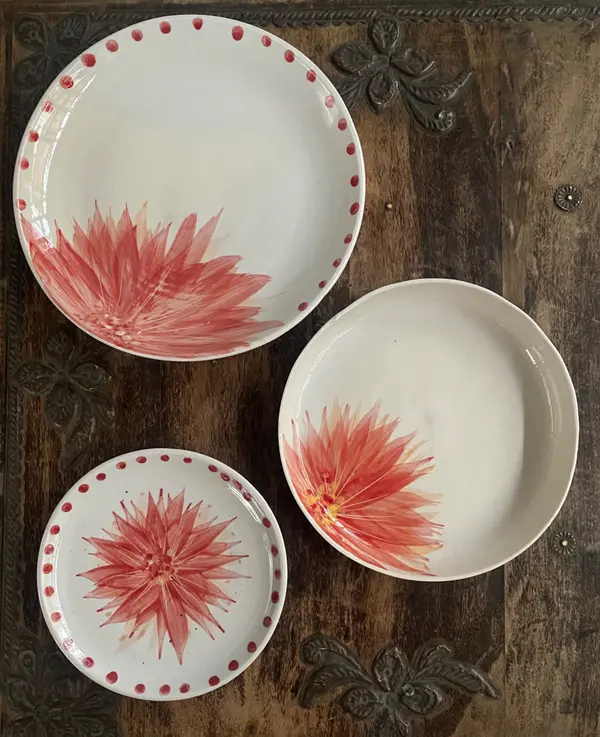 Set of three white ceramic plates and a bowl with hand-painted red dahlia floral designs on dark wood.