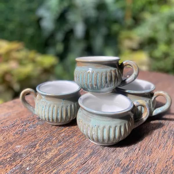 Four small fluted ceramic mugs with a light green glaze and brown highlights on a wooden surface.