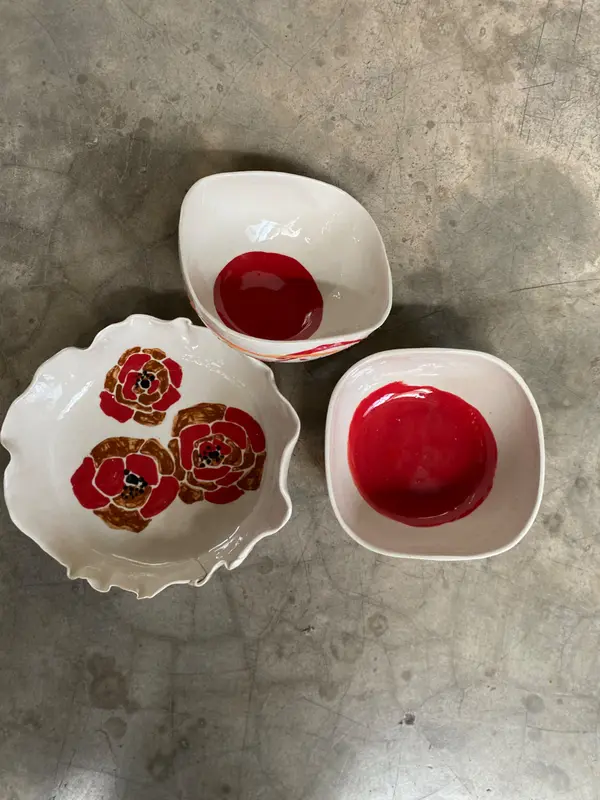 Three white ceramic bowls with bright red glaze centers and hand-painted poppy motifs on a gray concrete floor.