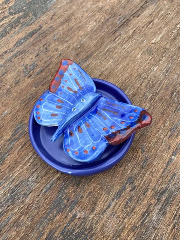 Cobalt blue ceramic butterfly with red wing details resting in a small round matching blue dish on wood.