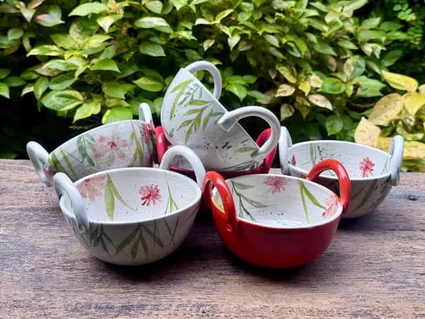 Five hand-painted ceramic bowls with handles, featuring botanical motifs on a speckled white and red glaze.