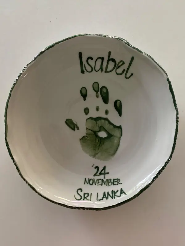 White ceramic bowl with a dark green handprint and hand-painted text: Isabel, 24 November, Sri Lanka.