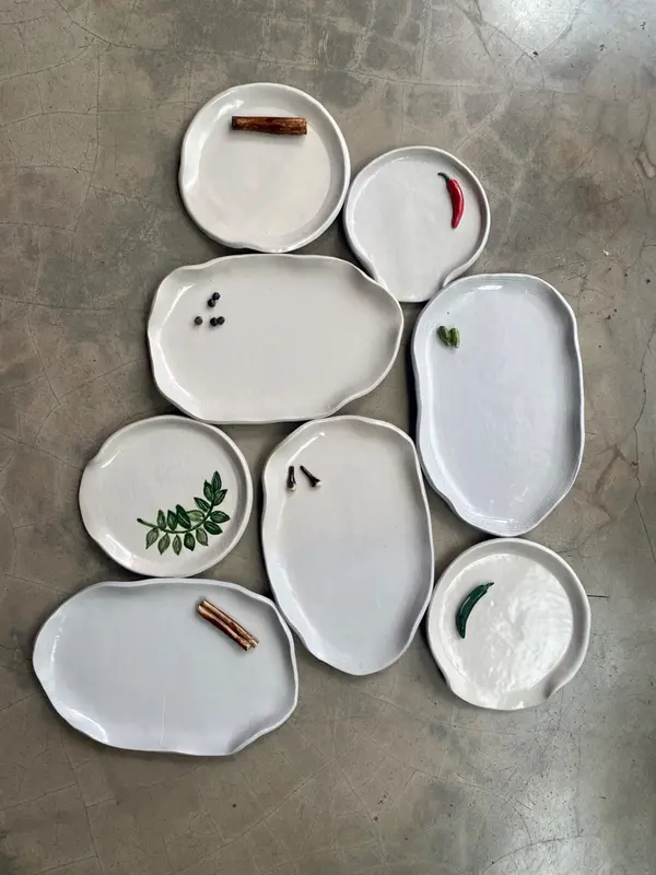 Collection of irregular white ceramic plates and platters with organic edges on a concrete floor.