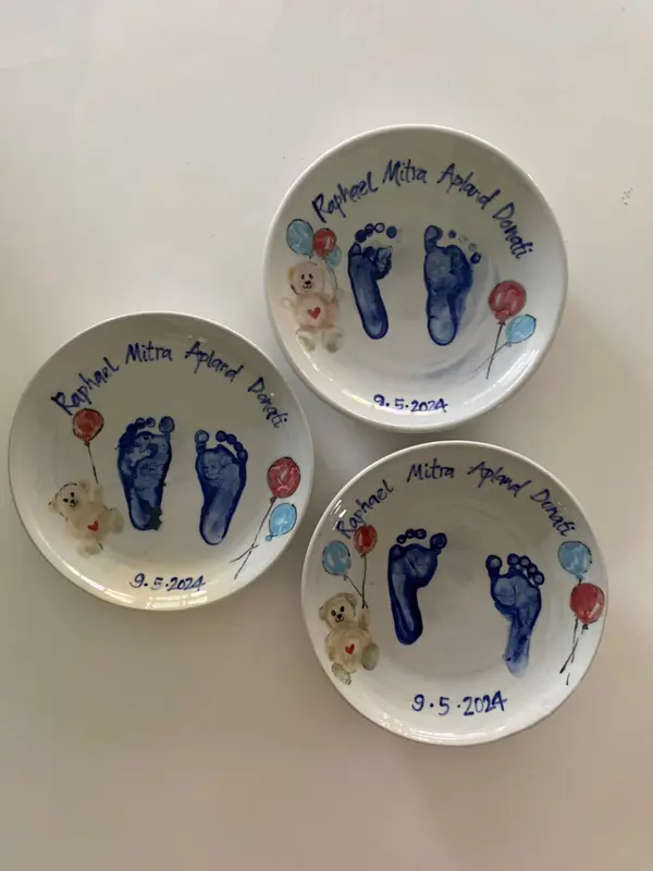 Three white ceramic bowls with blue baby footprints, hand-painted teddy bears, balloons, and handwritten inscriptions.