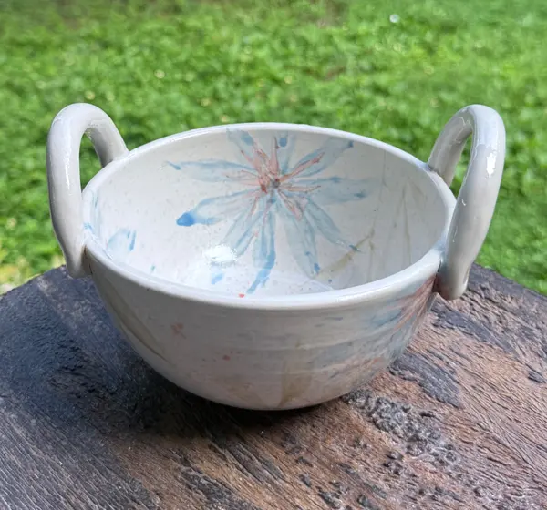 White ceramic bowl with two loop handles, decorated with hand-painted light blue and peach floral patterns.