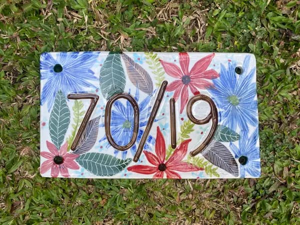 Rectangular ceramic house number plate with blue and red flowers and brown embossed digits 70/19.
