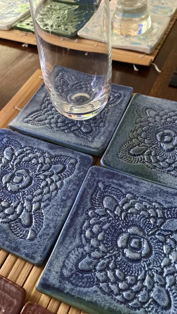 Four cobalt blue ceramic coasters with embossed floral patterns, one holding a clear glass of water.