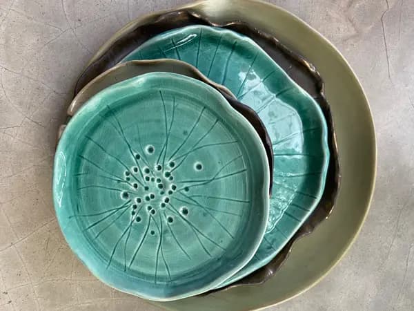 A stack of organic-edged ceramic plates in turquoise and sage, featuring a debossed lotus leaf design.