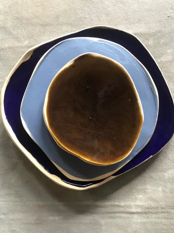 Three nested organic-shaped ceramic plates in dark cobalt, light blue, and amber glazes on a linen background.