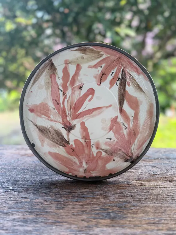 Round ceramic plate with hand-painted pink and brown floral motifs on a white glaze, shown on a wooden surface.