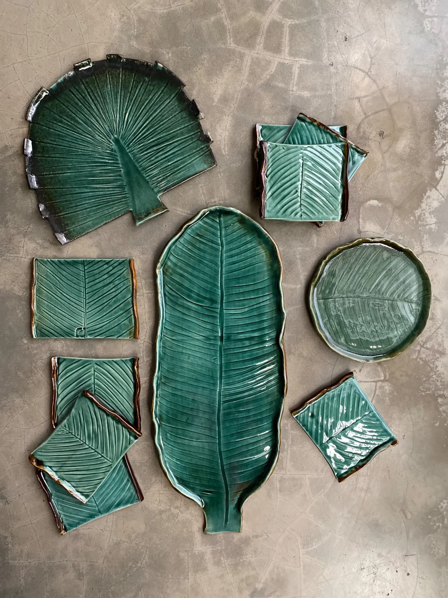 Set of green glazed ceramic platters and coasters in various leaf shapes on a grey surface.