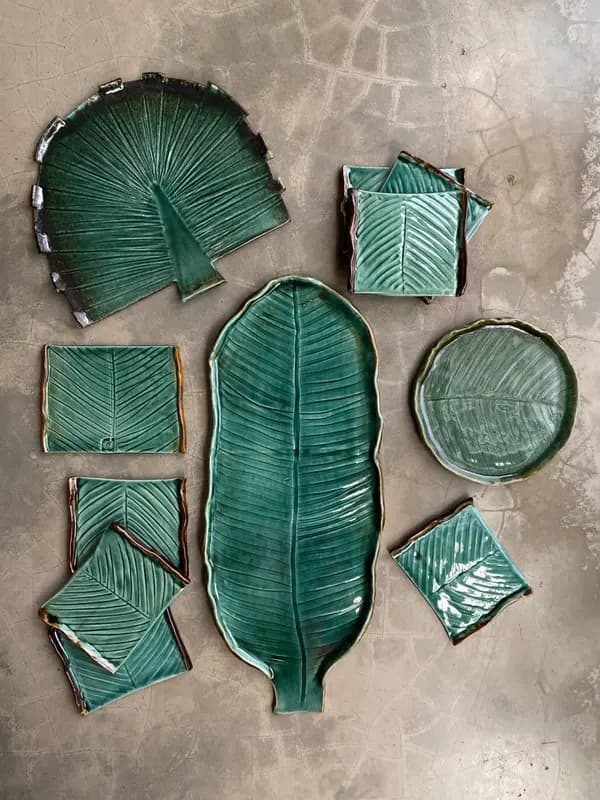 Set of green glazed ceramic platters and coasters in various leaf shapes on a grey surface.
