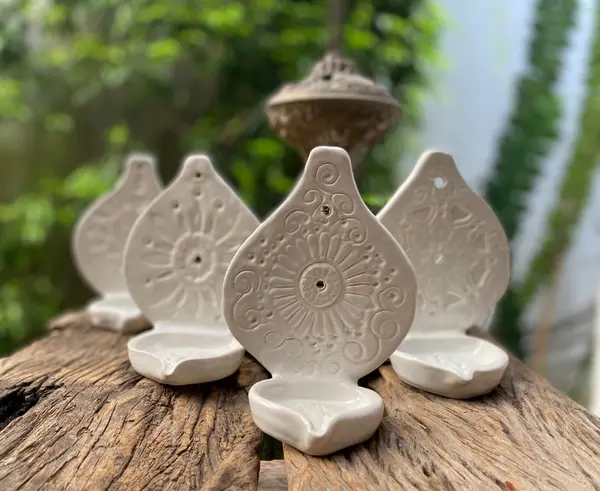 Four white glazed ceramic oil lamps with embossed floral mandala designs on a rustic wood surface.