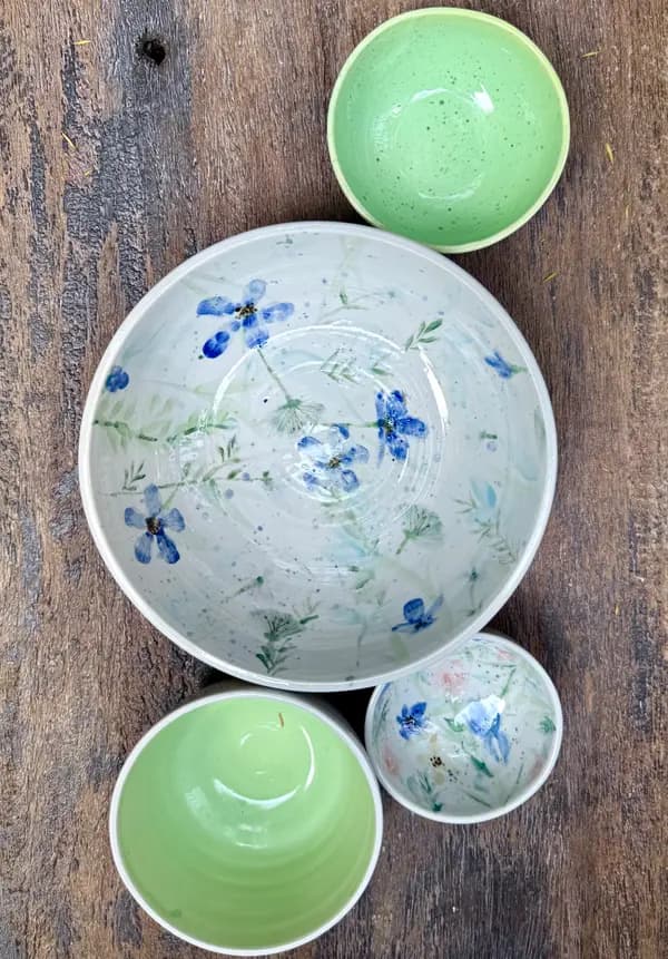 Four ceramic bowls on wood, two with lime green interiors and two with hand-painted blue floral designs.