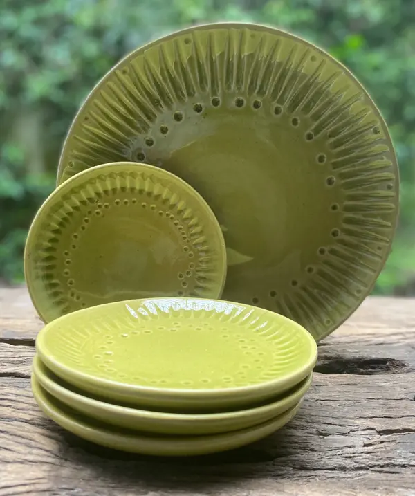 Set of apple green ceramic plates with radial textured rims on a rustic wooden surface.