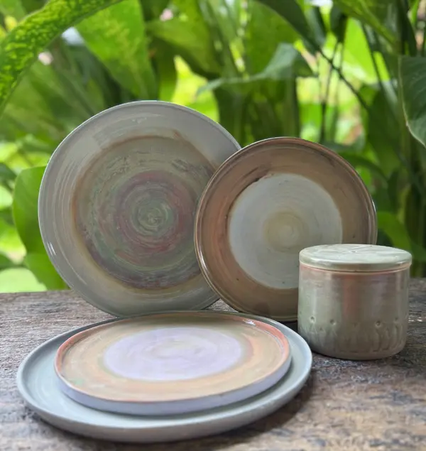 Handmade ceramic dinnerware set including three swirl-patterned plates and a lidded sage green jar on a wooden surface.