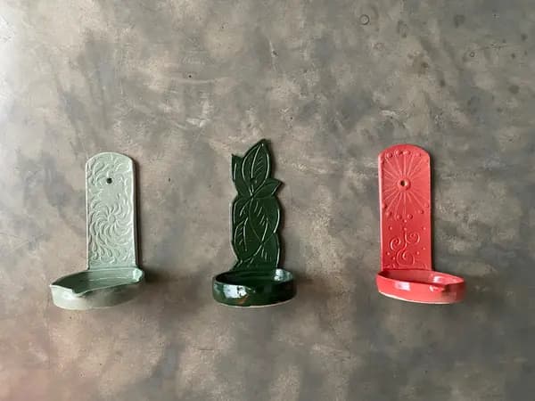 Three ceramic wall-mounted candle holders in sage green, dark green, and red with embossed botanical designs.