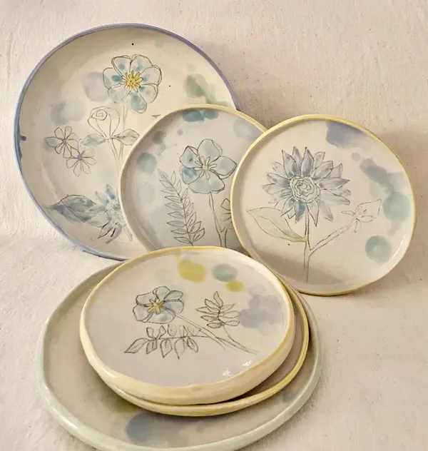 Arrangement of handmade ceramic plates featuring delicate hand-painted blue flowers and watercolor glaze accents.
