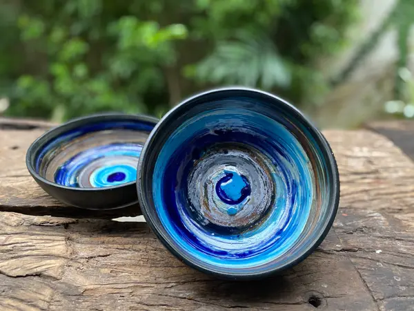 Two small black ceramic bowls with hand-painted blue and turquoise swirl interiors on a rustic wooden table.