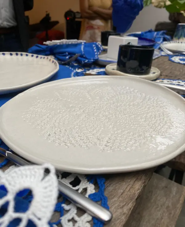 White ceramic plate with a circular lace-textured imprint, set on a wooden table with blue linens.