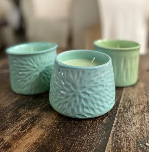 Three textured ceramic candle holders in shades of turquoise and light green on a rustic wooden table.