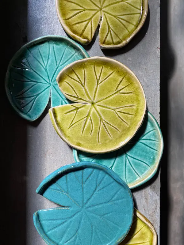 Ceramic lily pad-shaped plates in green and turquoise glazes with detailed leaf vein textures and crackle finish.