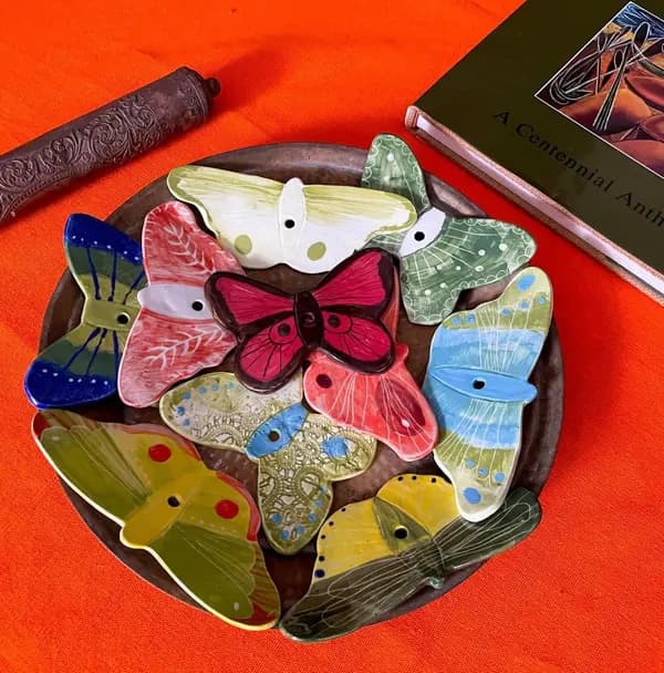 Colorful ceramic butterfly wall decorations in various glazes arranged on a dark circular plate.