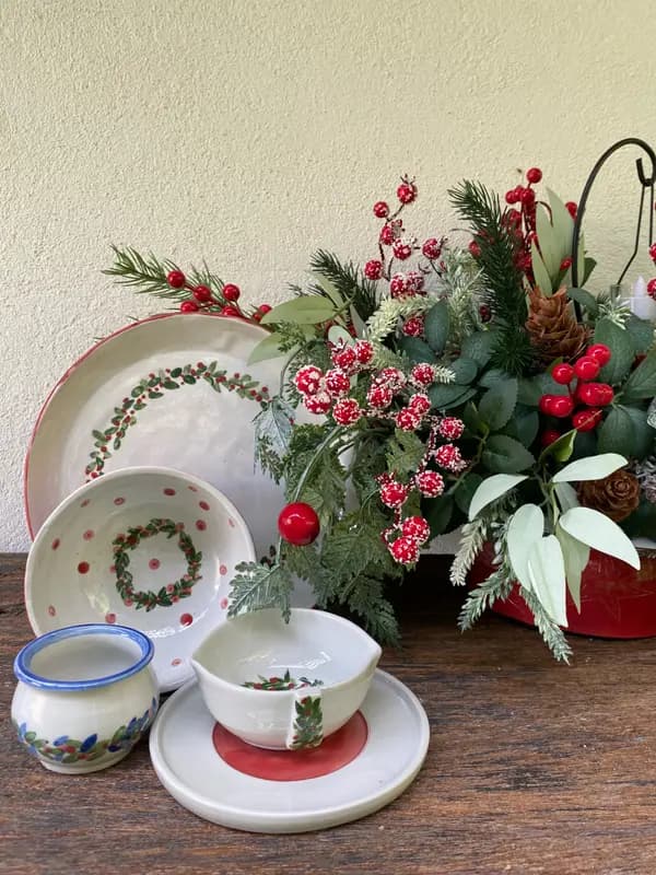 Festive white ceramic plate and bowl set with hand-painted red berry wreaths next to holiday greenery.