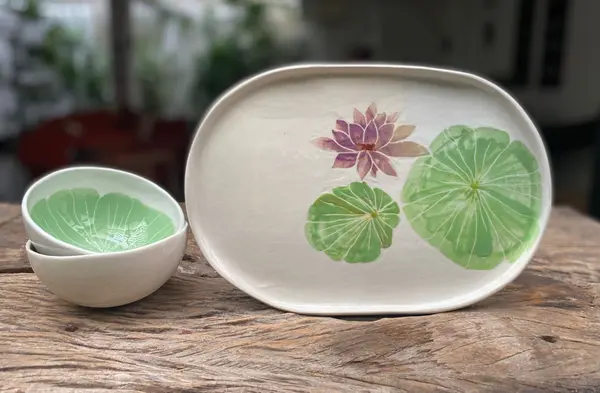 White ceramic platter and bowls featuring hand-painted lotus flower and lily pads on a wooden surface.