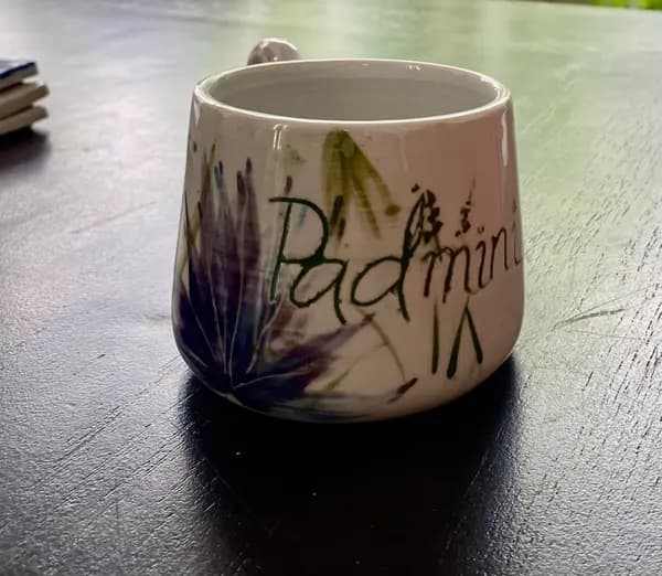 White ceramic mug with hand-painted purple flowers and the name Padmini in green script.