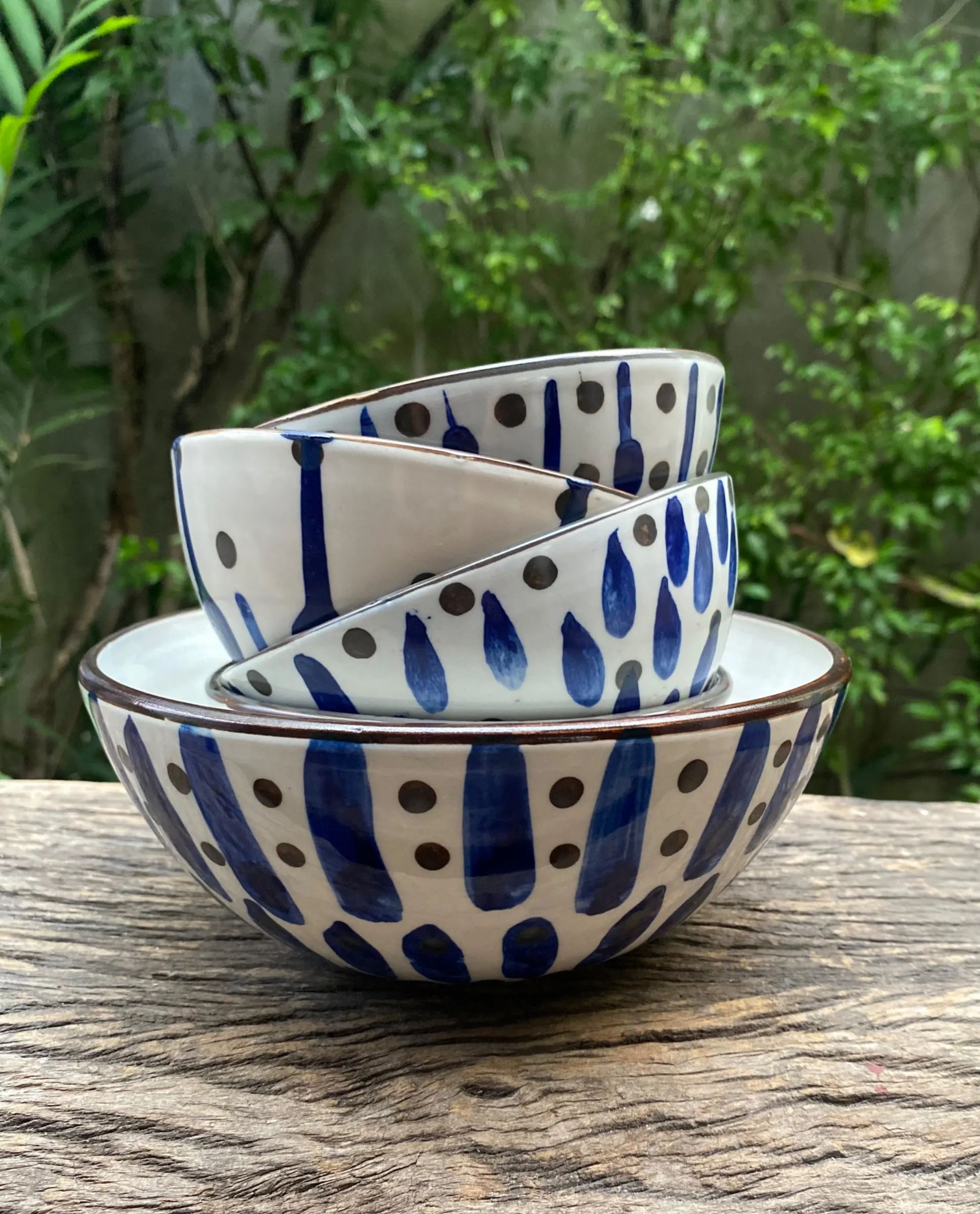 Three white ceramic bowls with hand-painted cobalt blue drops and brown dots stacked outdoors on wood.
