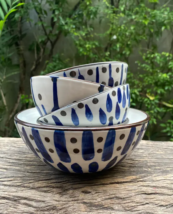 Three white ceramic bowls with hand-painted cobalt blue drops and brown dots stacked outdoors on wood.