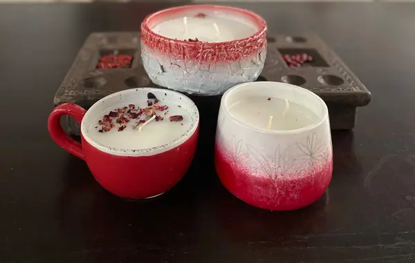 Three red and white ceramic candles with dried flower petals on a dark wood surface.