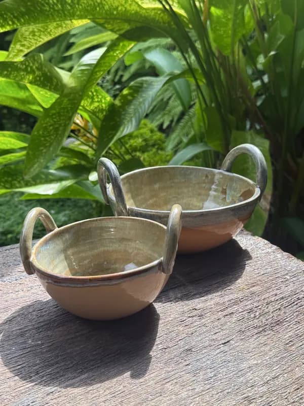 Two Brown Beige ceramic bowls with handles and sage green interiors on a rustic wooden table with garden background.