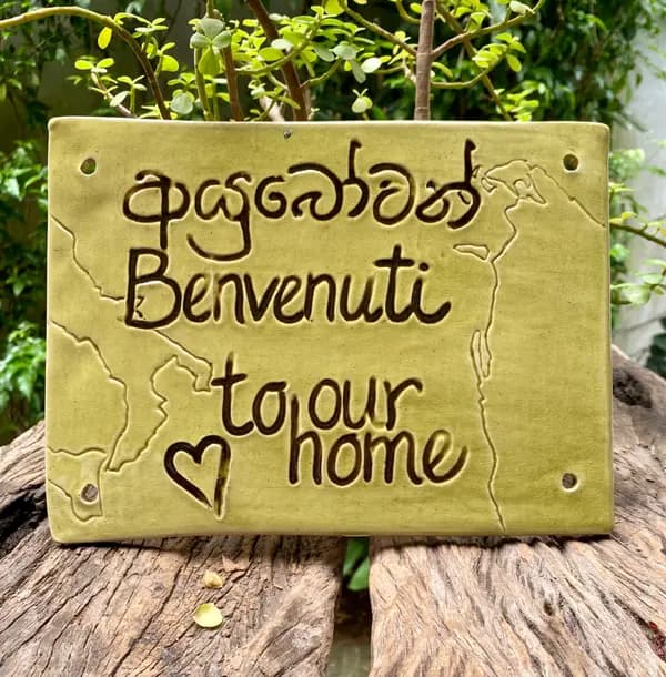 Apple green ceramic wall plaque with 'welcome' in Sinhala, Italian, and English, featuring etched map outlines.
