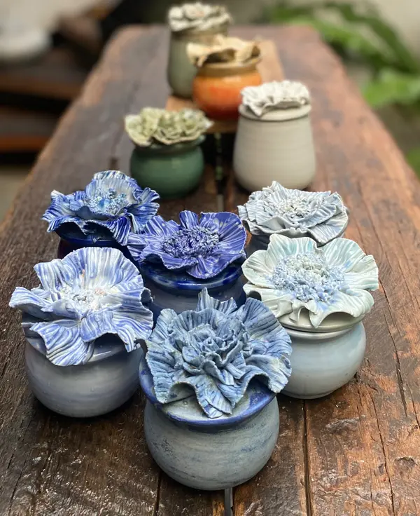 Ceramic jars with elaborate blue and white hand-sculpted flower lids arranged on a wooden table.