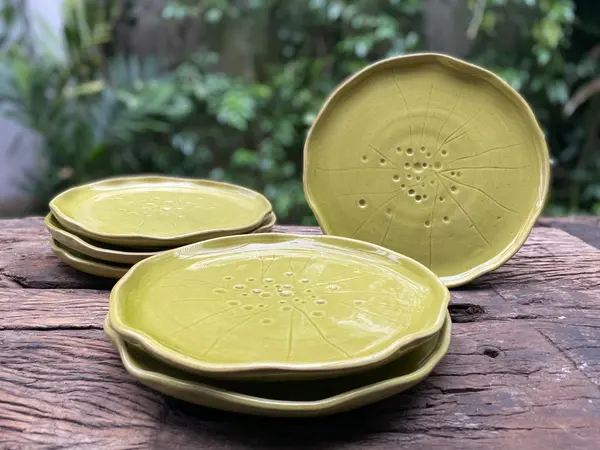 Handmade apple green ceramic plates with wavy rims and central radial line patterns on a wooden surface.