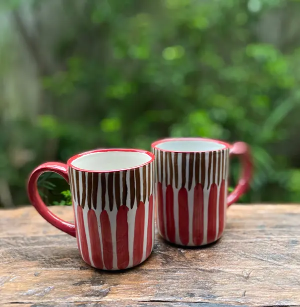 Two white ceramic mugs with red and brown vertical stripes on a rustic wooden table.