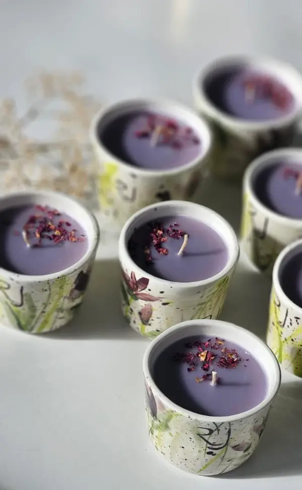 Hand-painted ceramic candle holders filled with purple wax and dried petals, featuring green and yellow floral motifs.