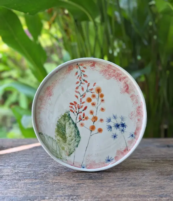 Round white ceramic plate with hand-painted botanical designs and a pink sponged border on a wooden table.