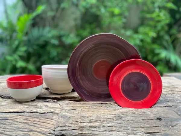 Hand-painted red and purple ceramic bowls and plates with spiral glaze on a rustic wood table.