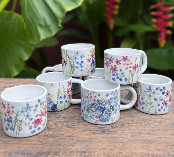Hand-painted white ceramic mugs with blue and red floral patterns, stacked on a wooden surface.