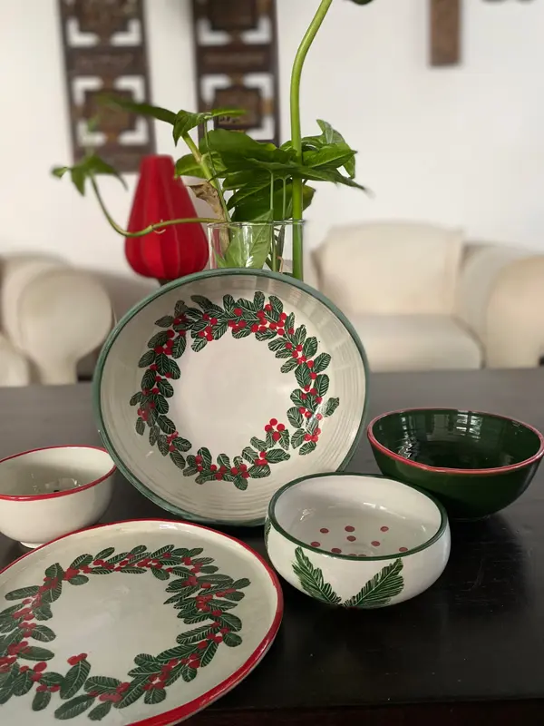 Hand-painted ceramic bowls and plate featuring a festive green wreath and red berries on a white glaze.