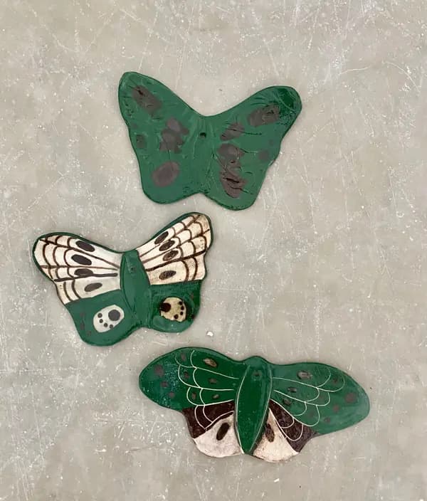 Three handcrafted ceramic butterfly wall hangings with dark green glazes and painted wing details.