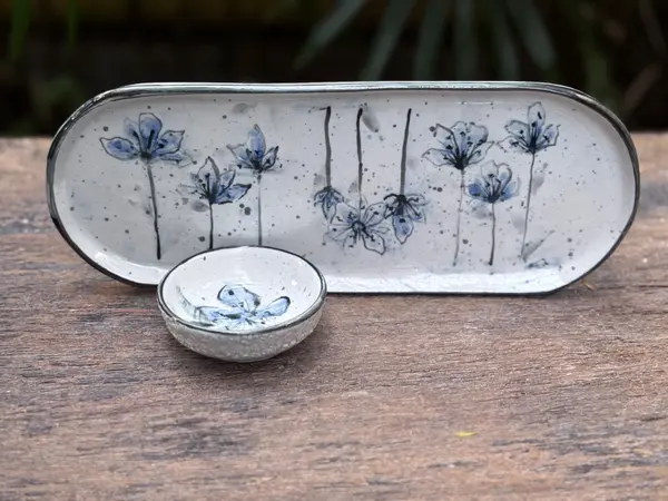 White ceramic platter and small dip bowl with hand-painted blue flowers and dark rims on a wooden surface.