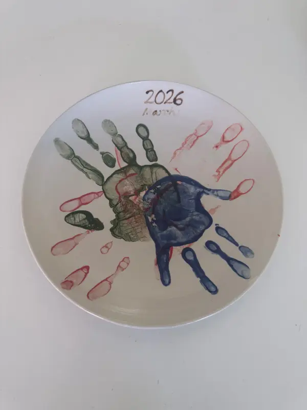 White ceramic plate with green and blue handprints and red outlines, dated 2026 March.