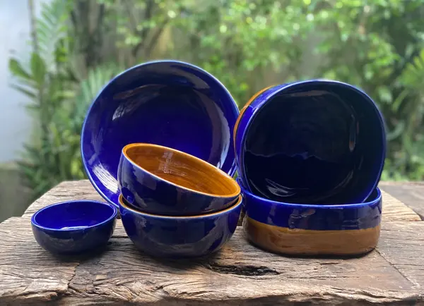 A set of cobalt blue and orange glazed ceramic bowls and a plate on a rustic wood table.